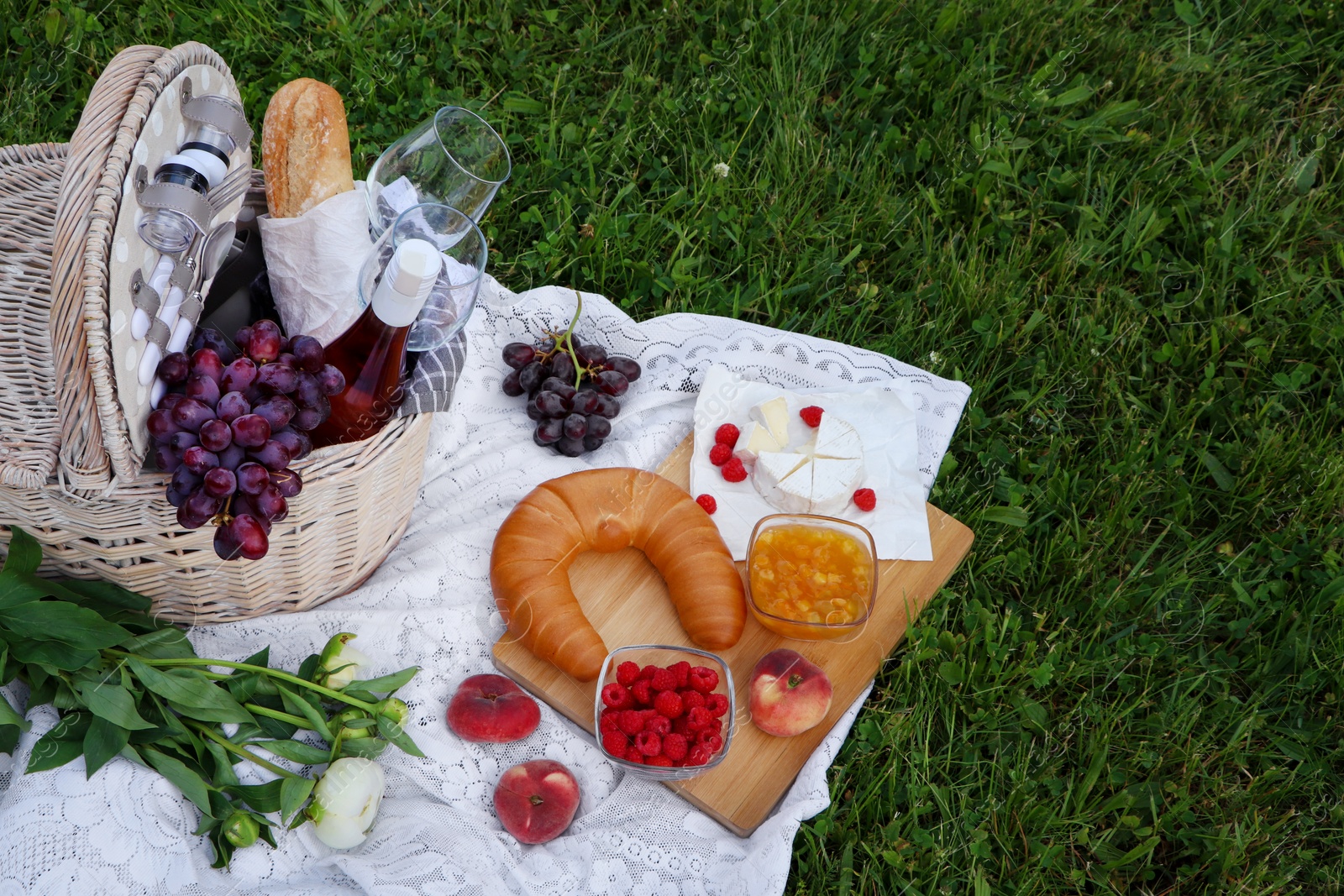 Photo of Picnic blanket with tasty food, flowers, basket and cider on green grass outdoors. Space for text