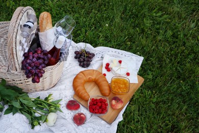 Picnic blanket with tasty food, flowers, basket and cider on green grass outdoors. Space for text