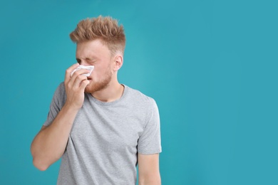 Photo of Young man suffering from allergy on blue background. Space for text