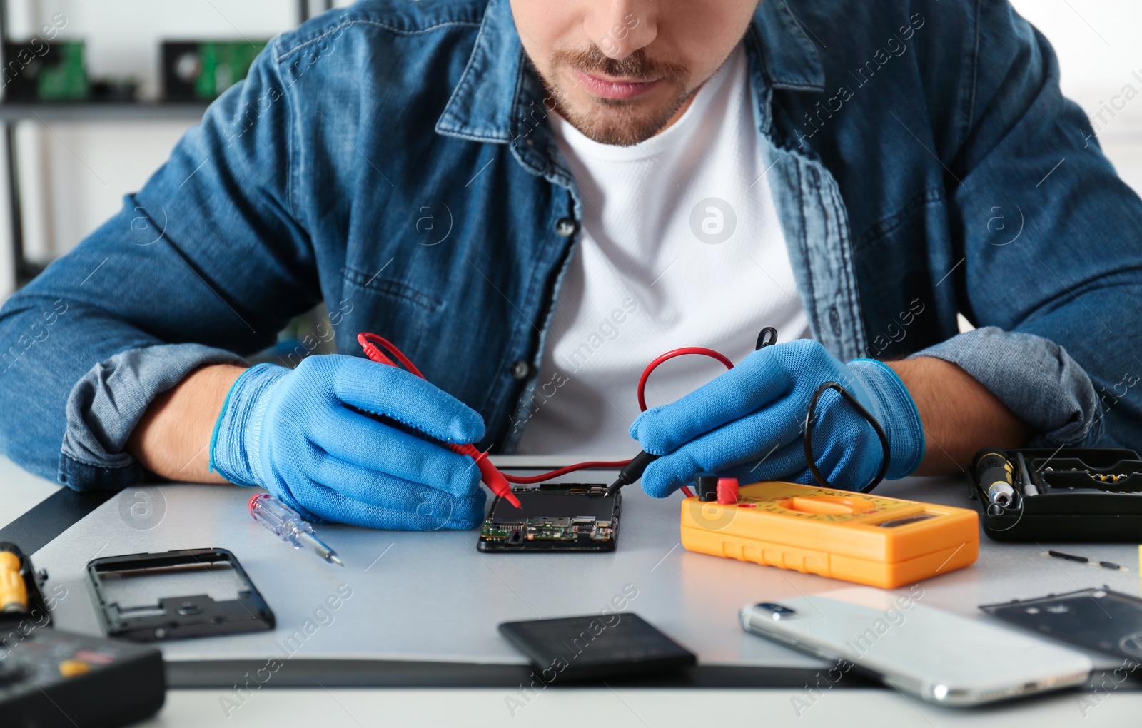 Photo of Technician checking broken smartphone at table in repair shop, closeup