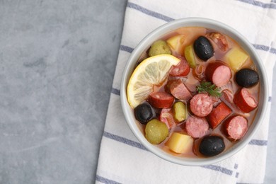 Photo of Meat solyanka soup with thin dry smoked sausages in bowl on grey table, top view. Space for text