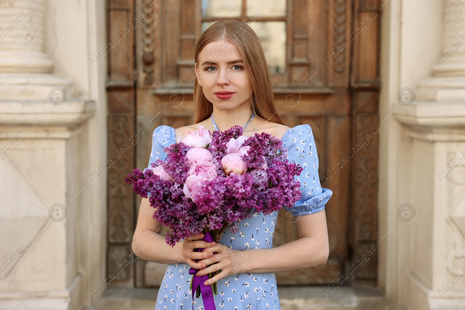 Photo of Beautiful woman with bouquet of spring flowers near building outdoors