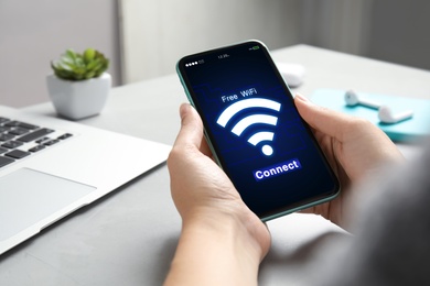 Image of Woman connecting to WiFi using mobile phone at table, closeup
