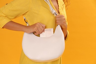 Young woman taking menstrual pad out of bag on yellow background, closeup
