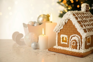 Photo of Beautiful gingerbread house decorated with icing and candles on white table