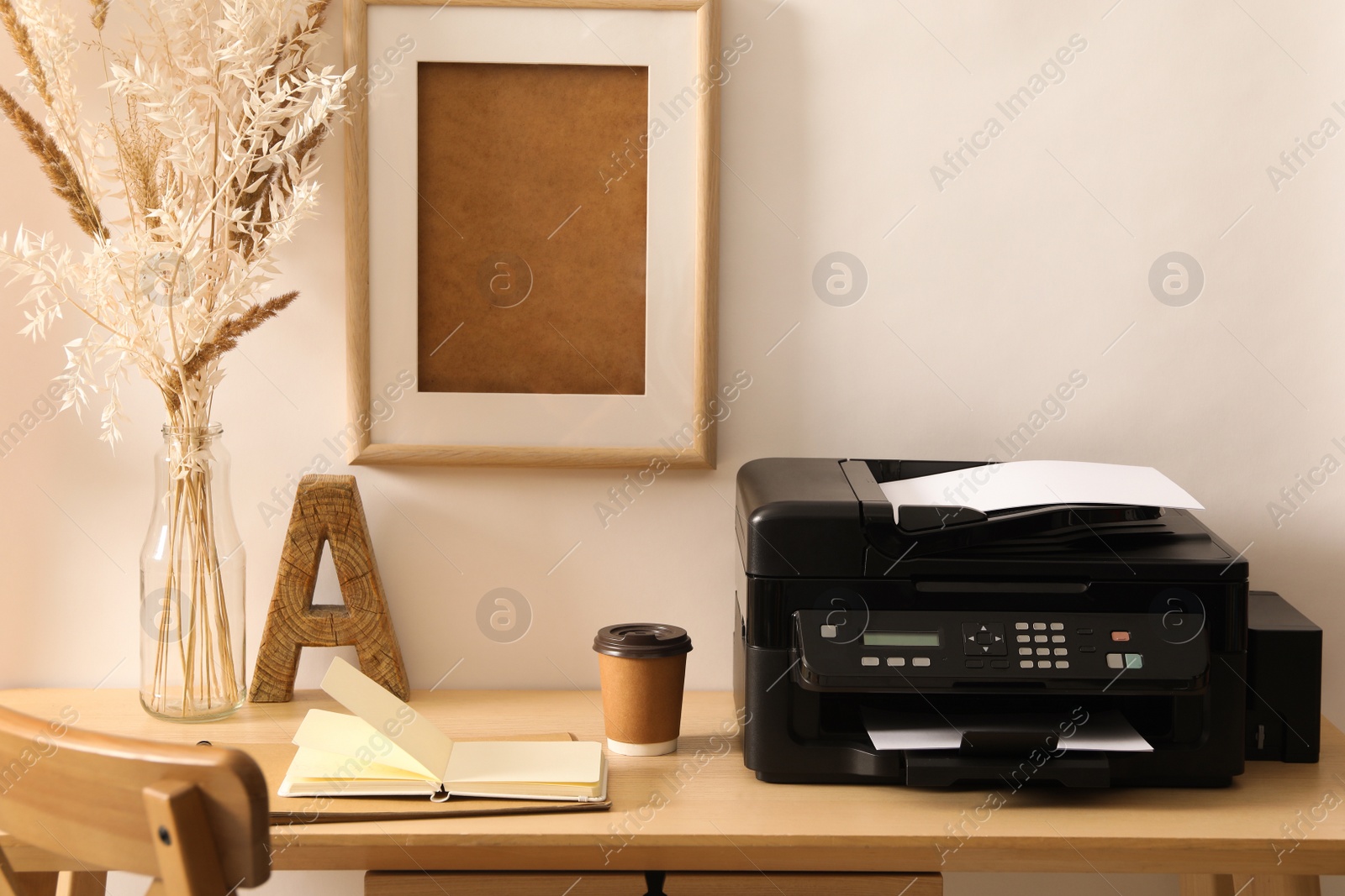 Photo of Modern printer with paper, notebook and cup of drink on wooden table indoors