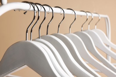 Photo of White clothes hangers on metal rack against beige background, closeup