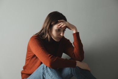 Photo of Sad young woman near grey wall indoors