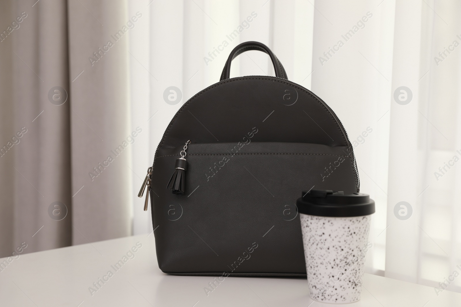 Photo of Stylish black backpack and cup of coffee on white table indoors