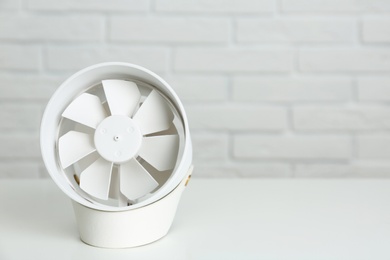 Photo of Portable fan on table near white brick wall, space for text. Summer heat