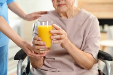 Photo of Nurse giving glass of juice to elderly woman indoors, closeup. Assisting senior people
