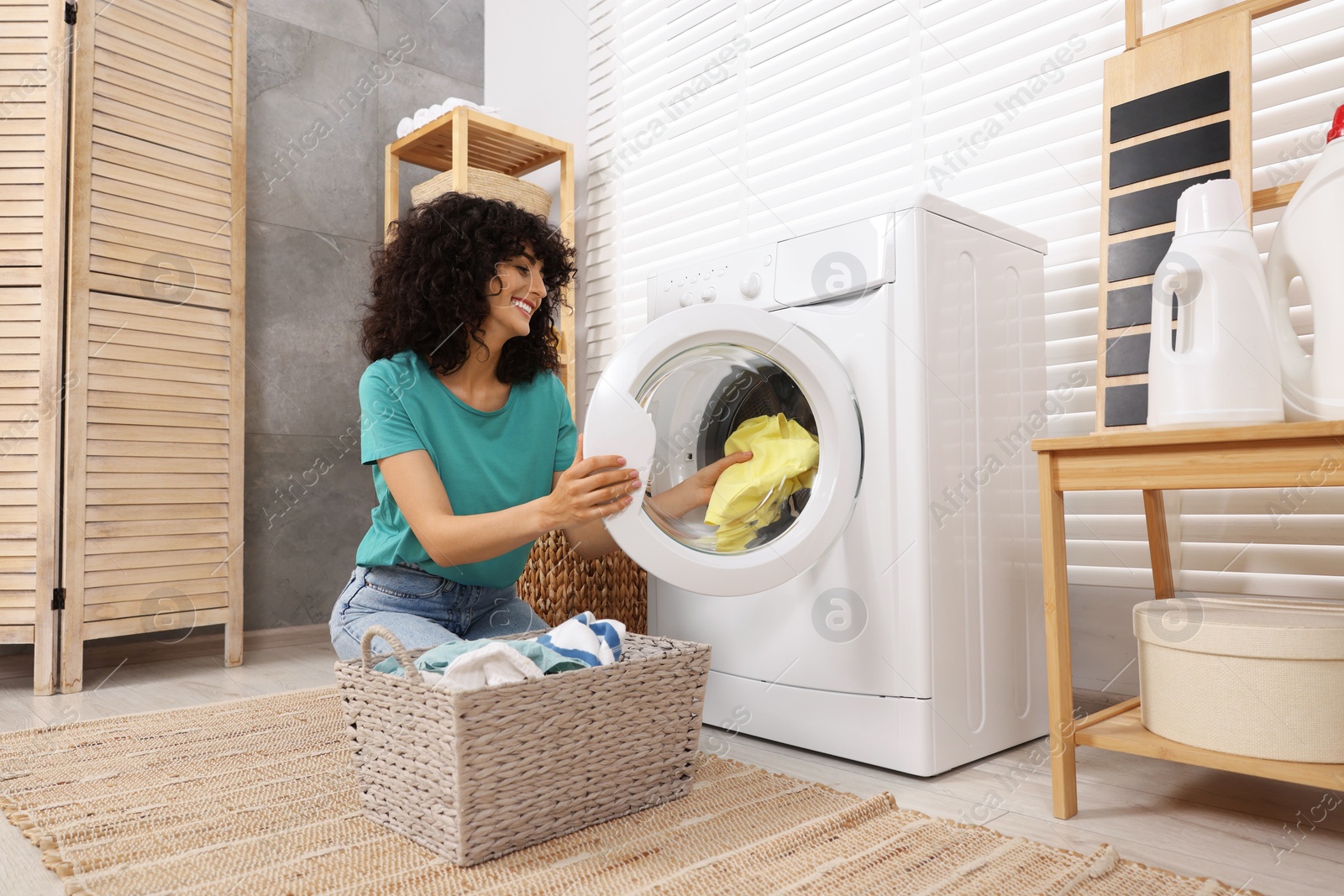 Photo of Happy woman putting laundry into washing machine indoors