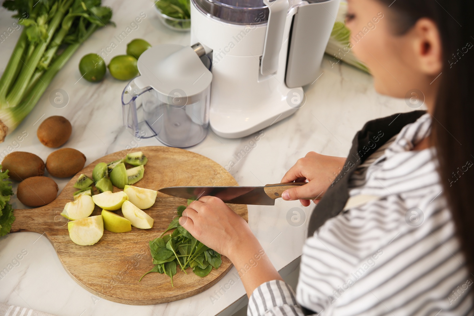 Photo of Young woman cutting fresh spinach for juice at table in kitchen