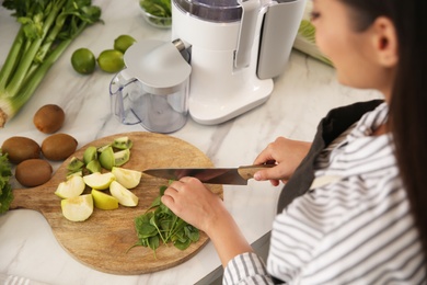 Photo of Young woman cutting fresh spinach for juice at table in kitchen