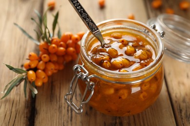 Delicious sea buckthorn jam and fresh berries on wooden table, closeup