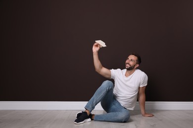 Handsome man playing with paper plane near brown wall. Space for text
