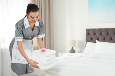 Photo of Chambermaid putting fresh towels on bed in hotel room. Space for text