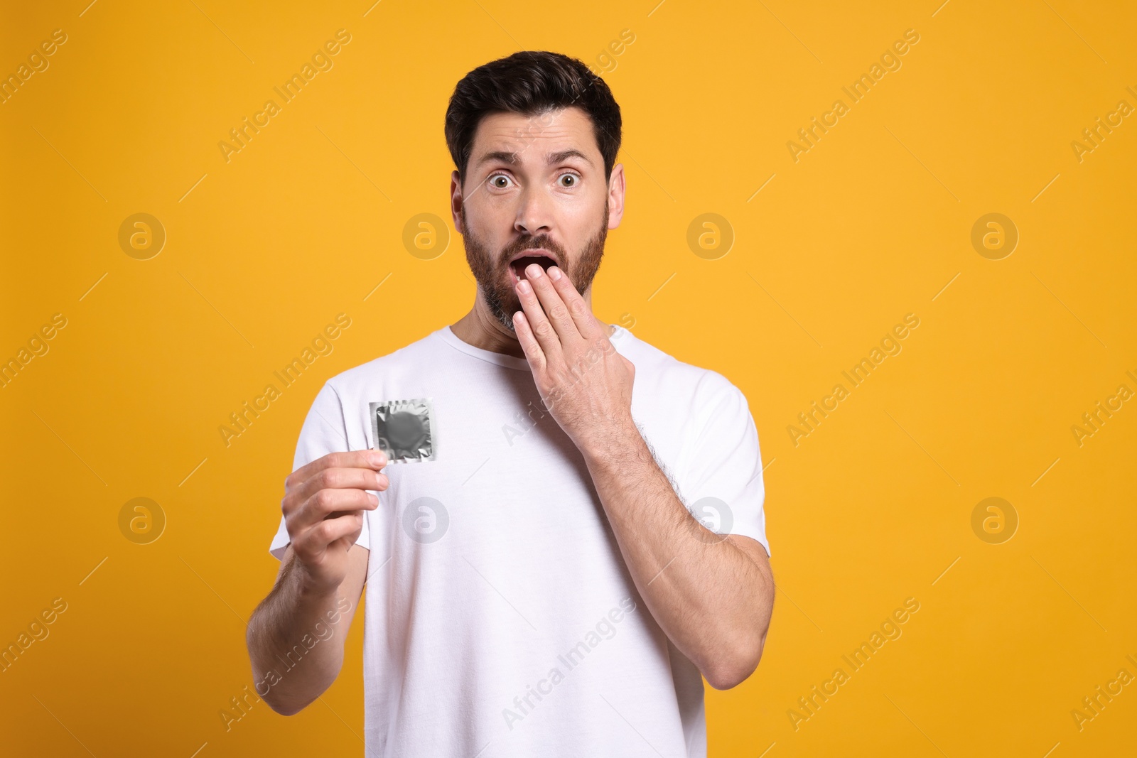 Photo of Emotional man holding condom on yellow background. Safe sex