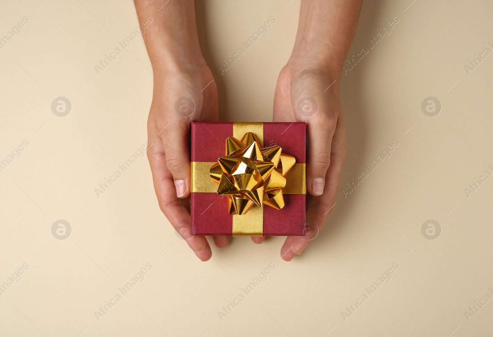 Photo of Woman holding beautiful gift box on beige background, top view