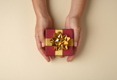 Photo of Woman holding beautiful gift box on beige background, top view