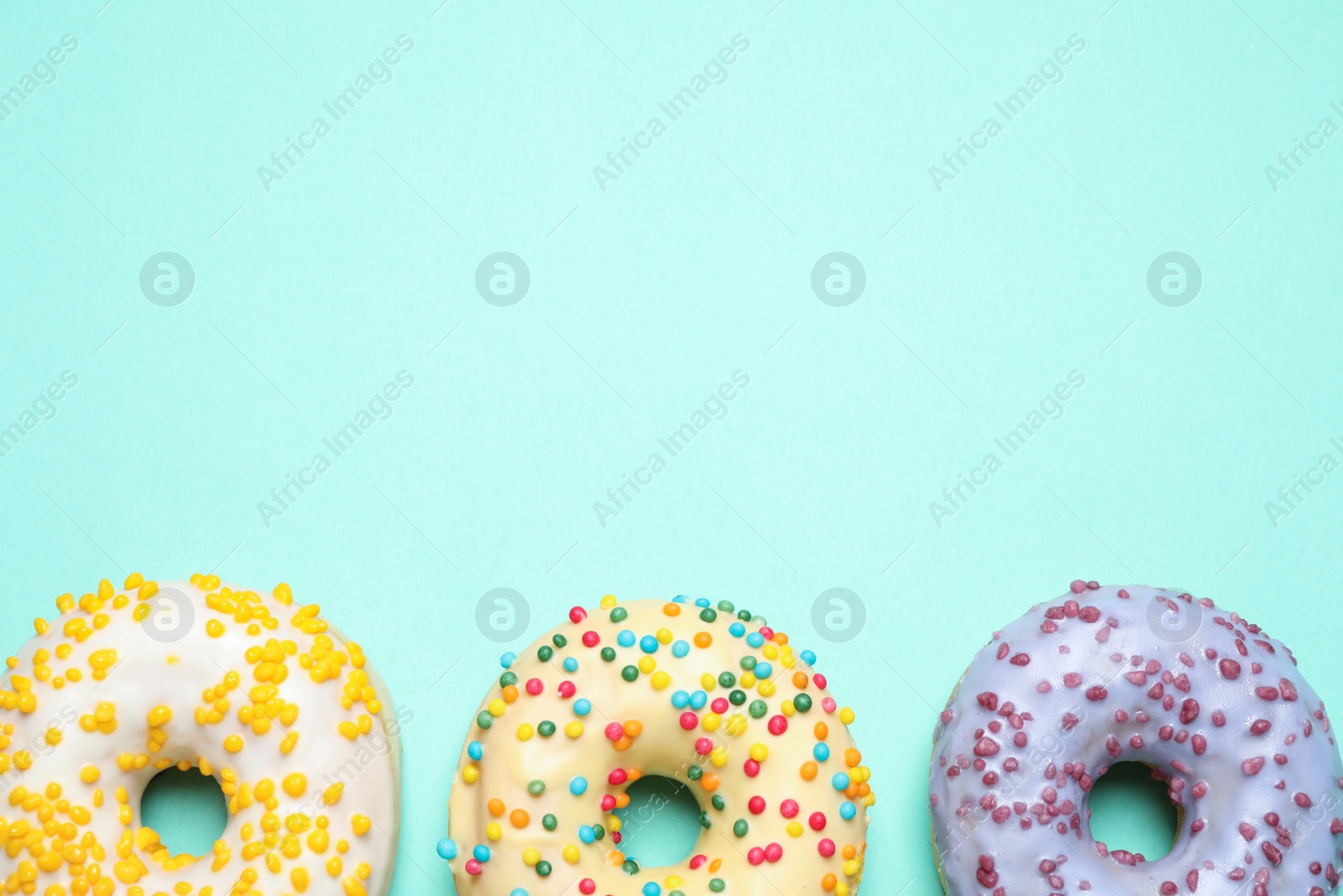 Photo of Delicious glazed donuts on turquoise background, flat lay. Space for text