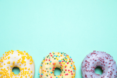 Photo of Delicious glazed donuts on turquoise background, flat lay. Space for text