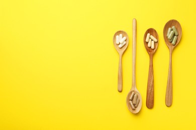 Photo of Different vitamin capsules in spoons on yellow background, flat lay. Space for text