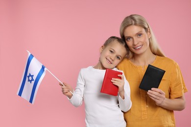 Photo of Immigration. Happy woman with her daughter holding passports and flag of Israel on pink background