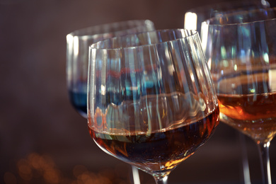 Elegant glasses with different wines on brown background, closeup