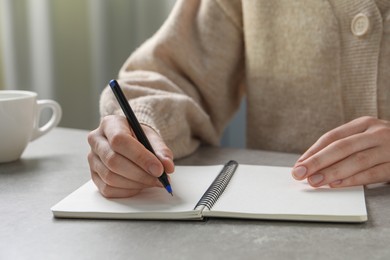 Photo of Woman with pen and notepad at grey table, closeup