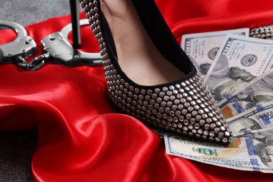 Prostitution concept. High heeled shoe, dollar banknotes and handcuffs on red cloth, closeup