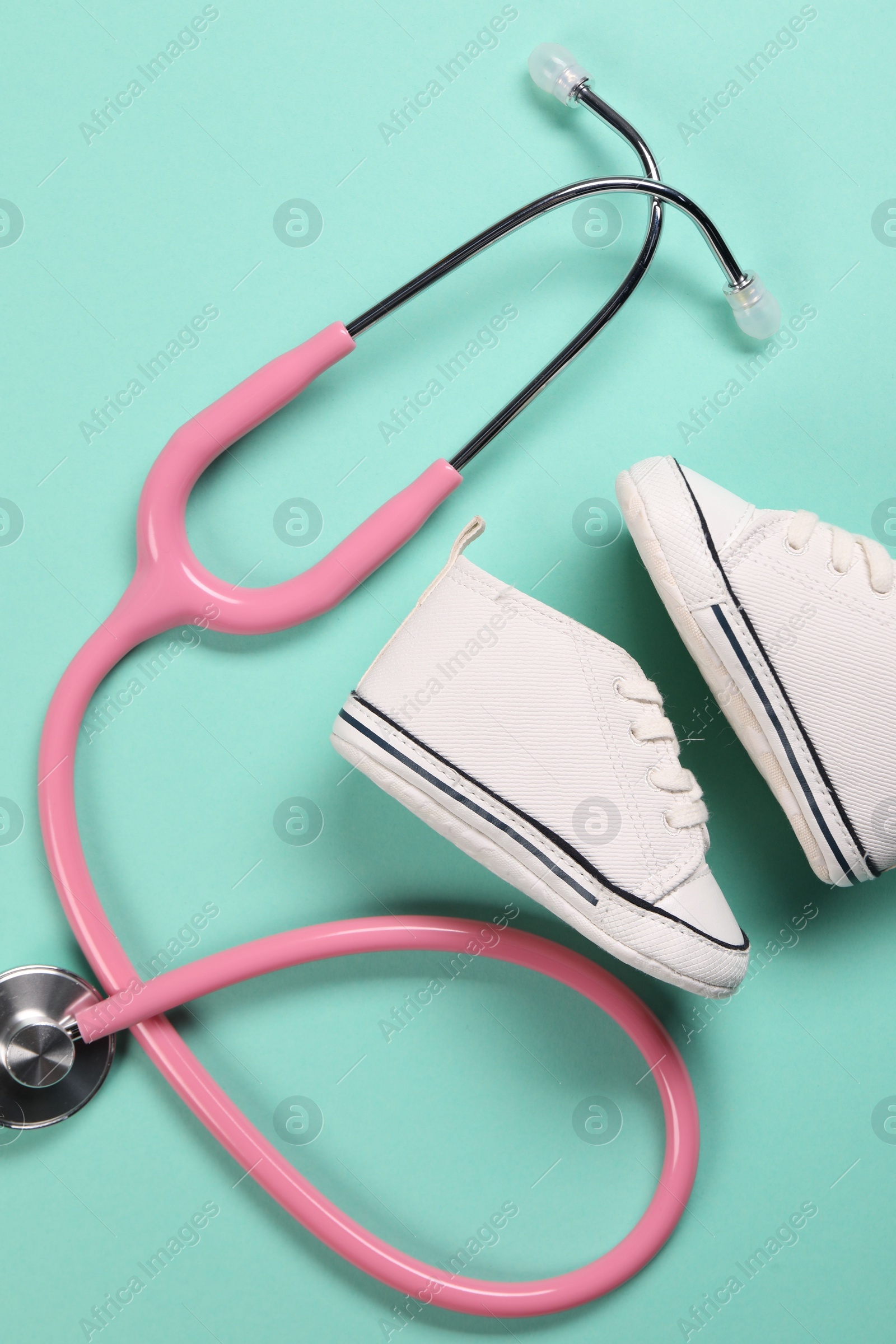 Photo of Stethoscope and kid's sneakers on turquoise background, flat lay