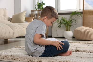 Photo of Boy with poor posture reading book on beige carpet in living room. Symptom of scoliosis