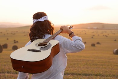 Photo of Hippie man with guitar in field, back view. Space for text