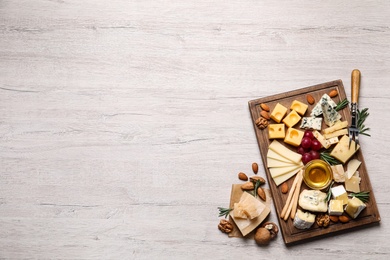Cheese plate with honey, grapes and nuts on white table, flat lay. Space for text