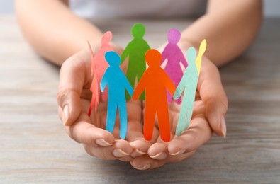 Photo of Woman holding paper human figures at wooden table, closeup. Diversity and inclusion concept
