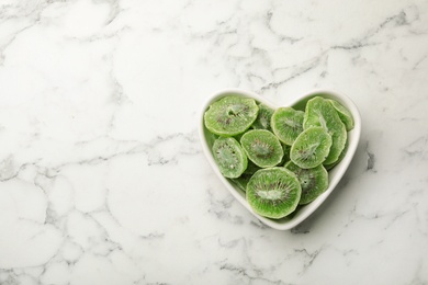 Photo of Bowl of dried kiwi on marble background, top view with space for text. Tasty and healthy fruit