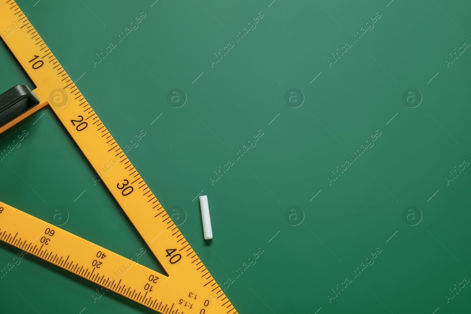 Photo of Yellow triangle and chalk on green chalkboard, flat lay. Space for text