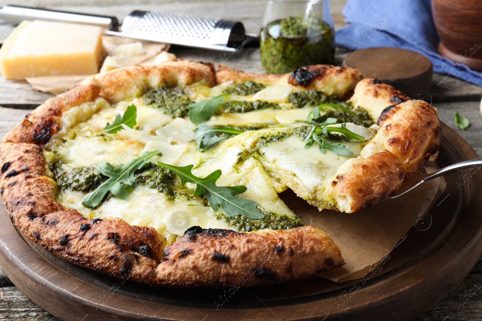 Photo of Taking slice of delicious pizza with pesto, cheese and arugula on wooden table, closeup