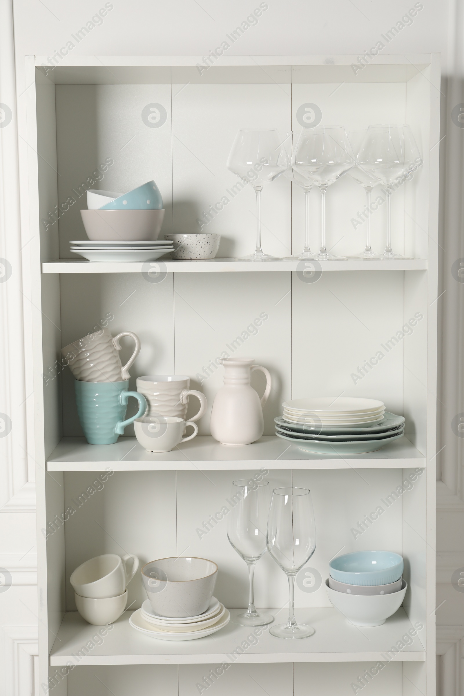 Photo of Different clean dishware and glasses on shelves in cabinet indoors