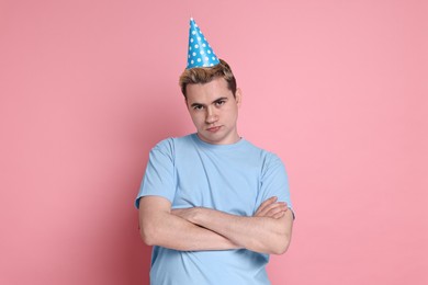 Sad young man with party hat on pink background