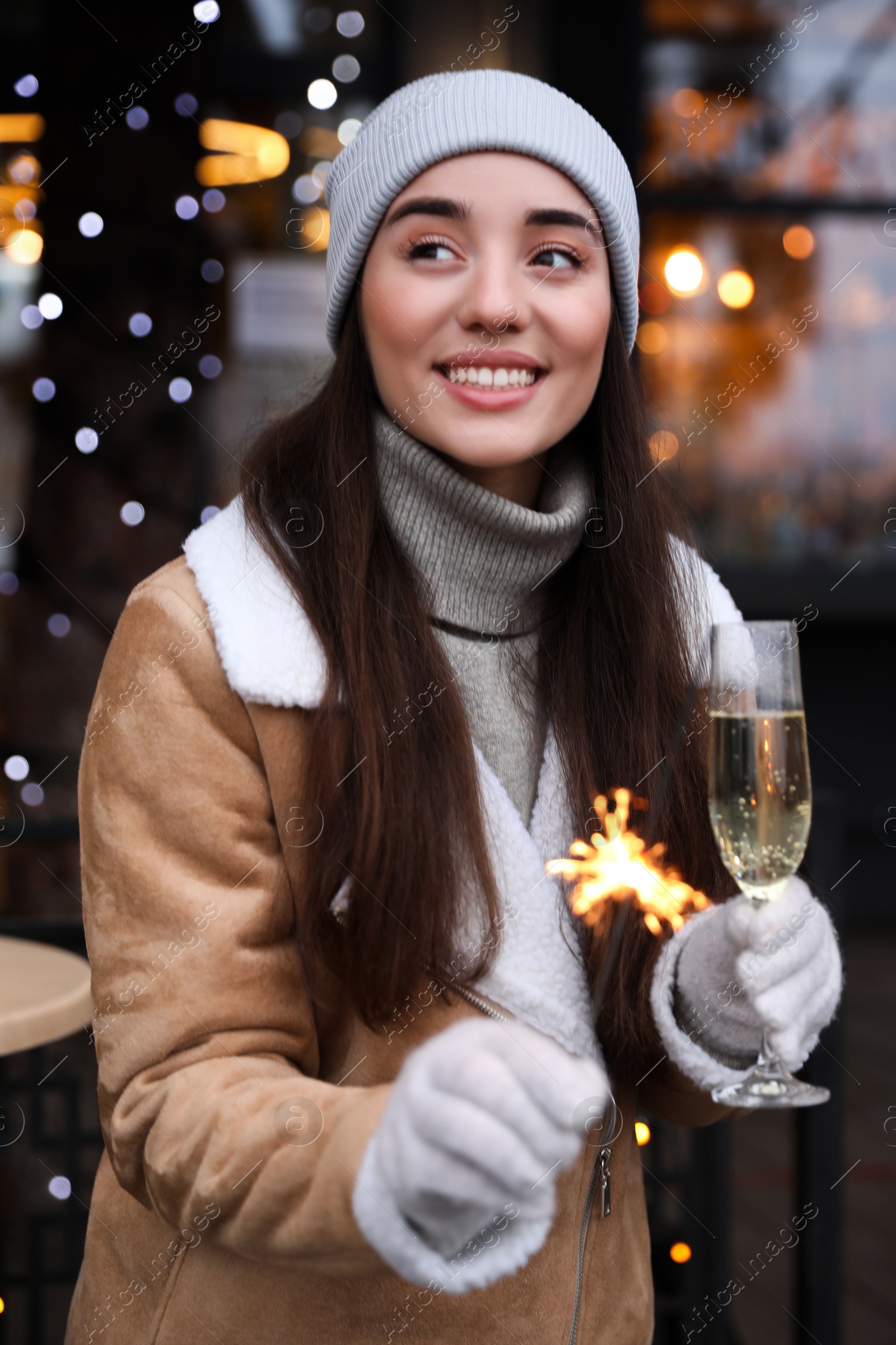 Photo of Happy young woman with sparkler and glass of champagne at winter fair