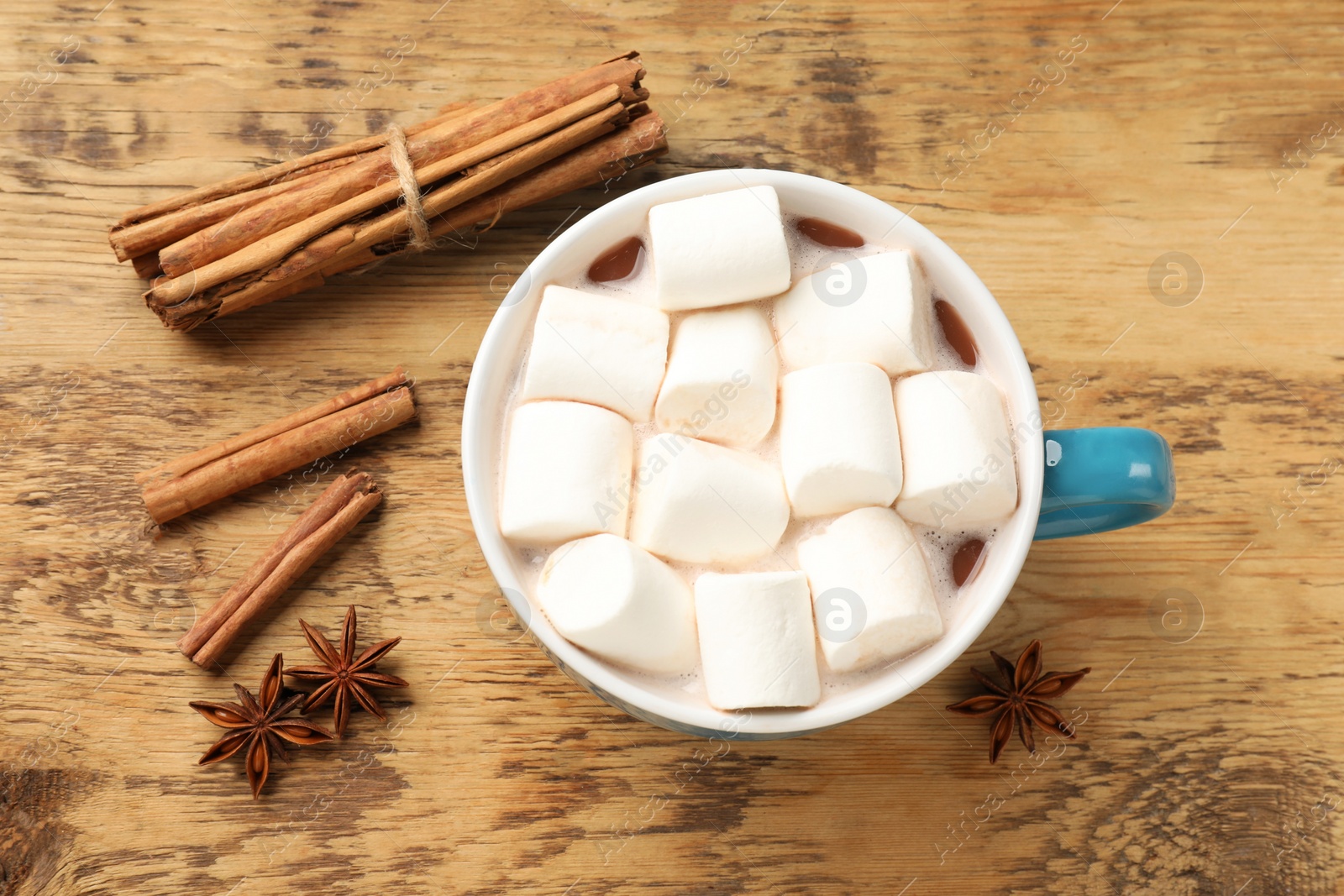 Photo of Tasty hot chocolate with marshmallows and spices on wooden table, flat lay