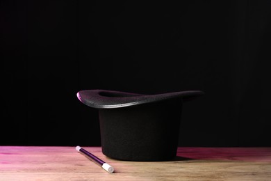 Photo of Magician's hat and wand on wooden table against black background