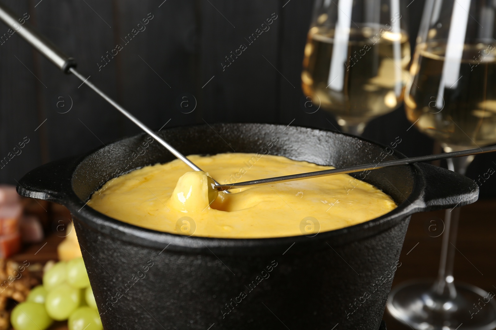 Photo of Dipping different products into fondue pot with melted cheese, closeup