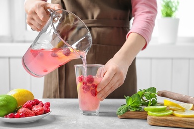 Woman pouring delicious lemonade into glass on table