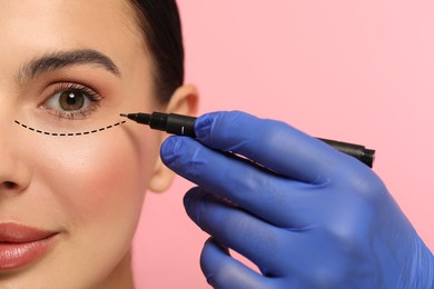 Image of Woman preparing for cosmetic surgery, pink background. Doctor drawing markings on her face, closeup