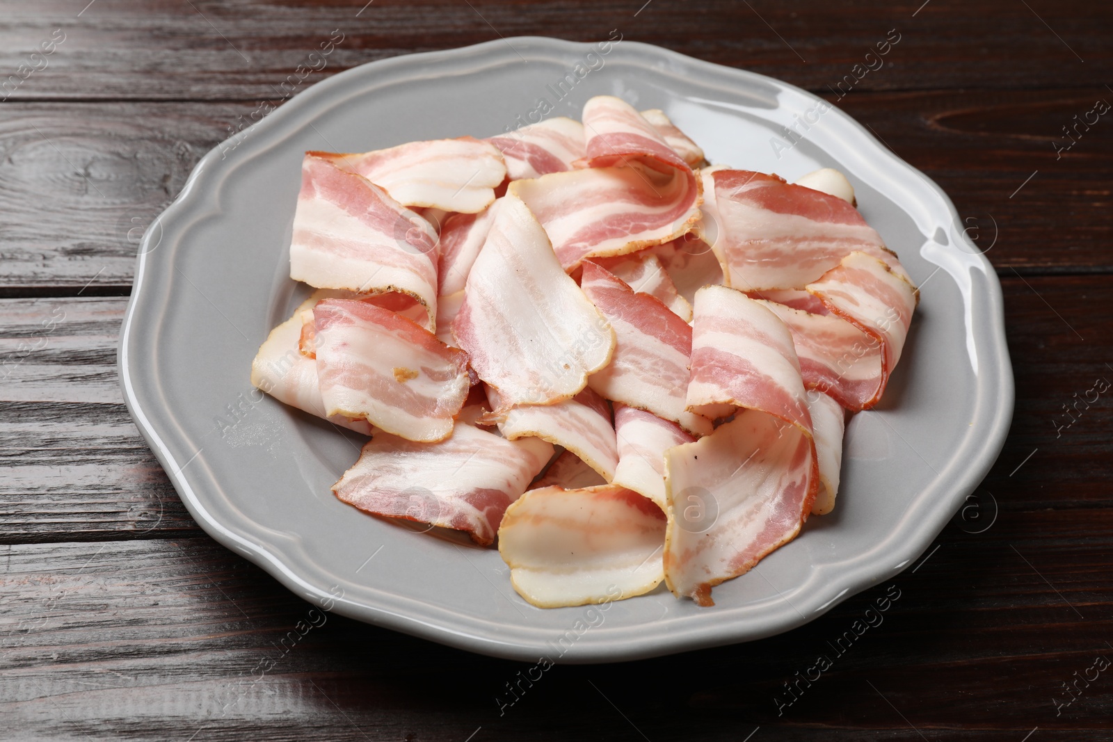 Photo of Slices of raw bacon on dark wooden table, closeup