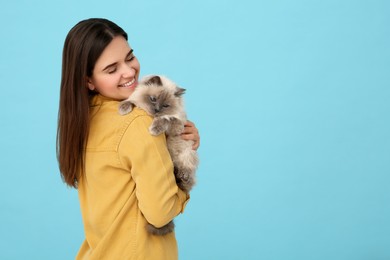 Photo of Happy woman with her cute cat on light blue background, space for text