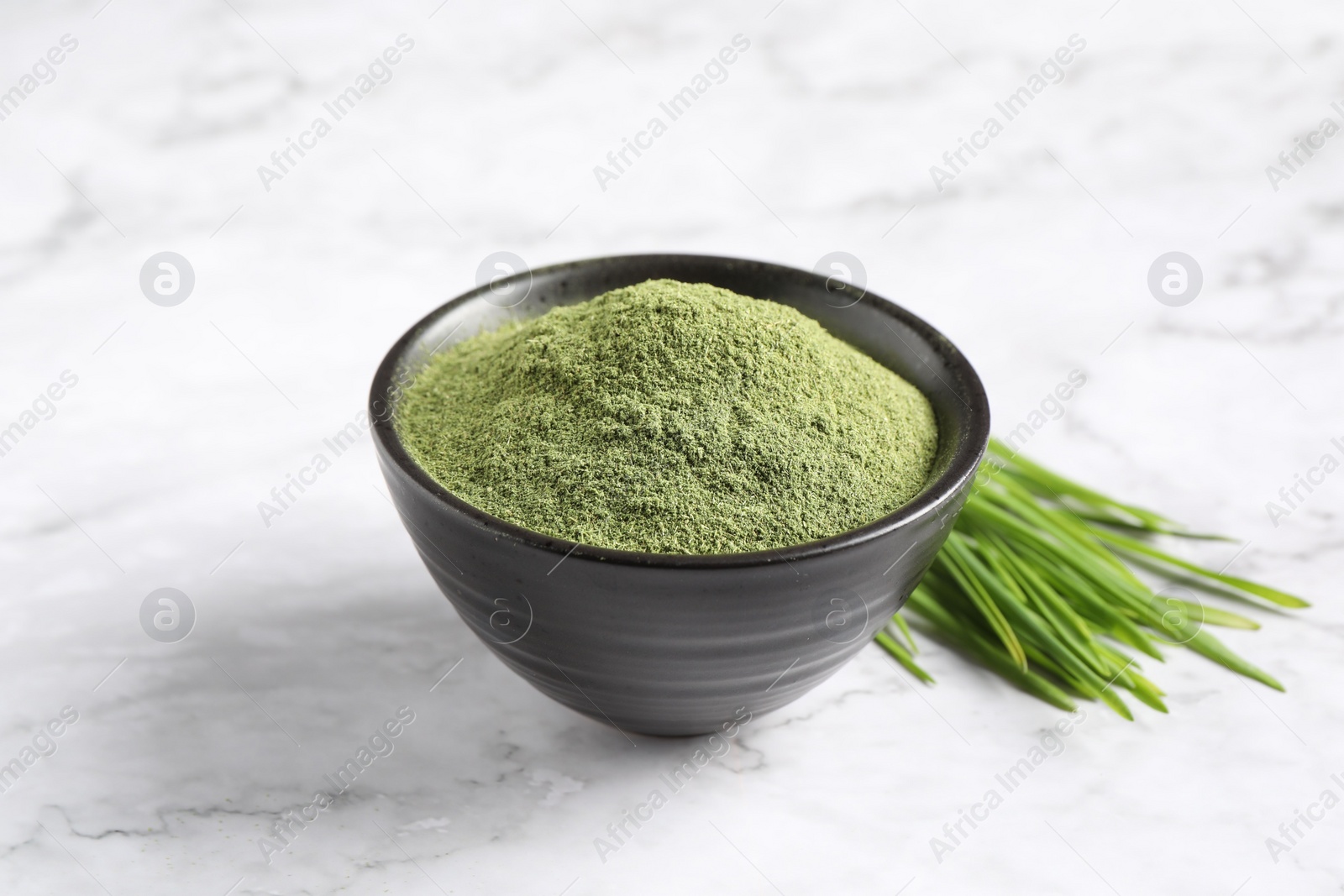 Photo of Wheat grass powder in bowl and fresh sprouts on white marble table, closeup